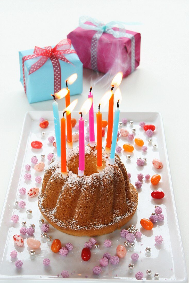 Geburtstagskuchen mit brennenden Kerzen beim Auspusten, Geschenkpäckchen
