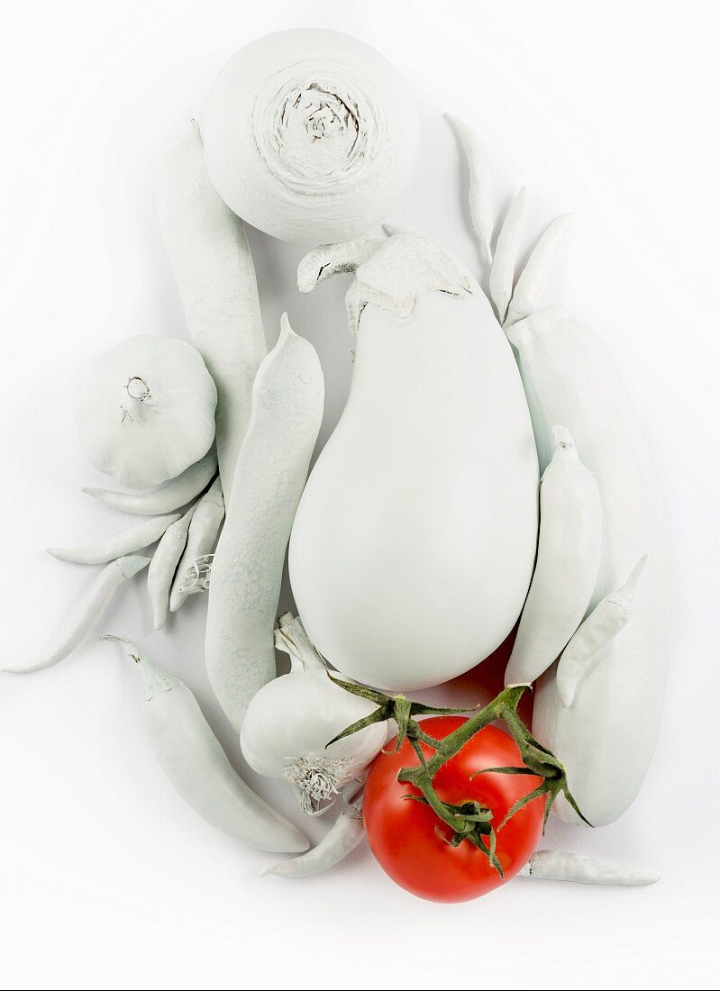 A still life in white, featuring vegetables, with a red tomato