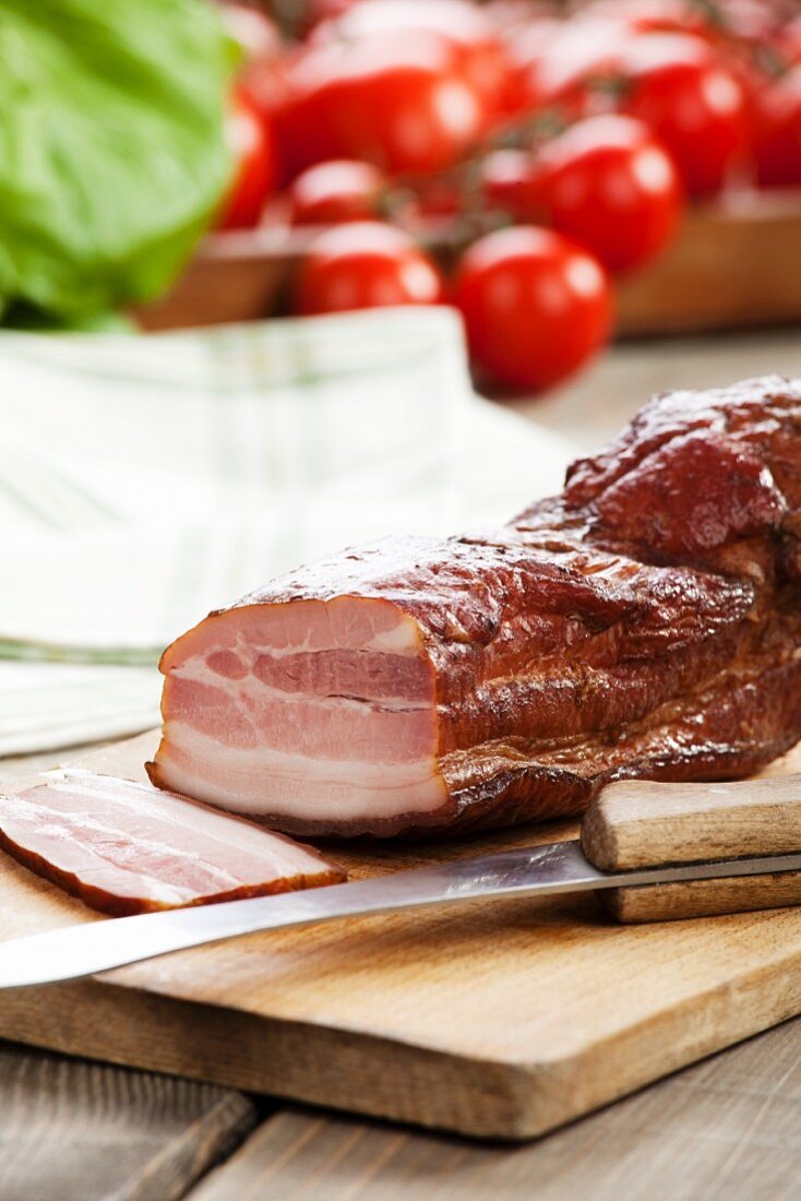 Partly sliced Speck ham with a sharp knife on a chopping board