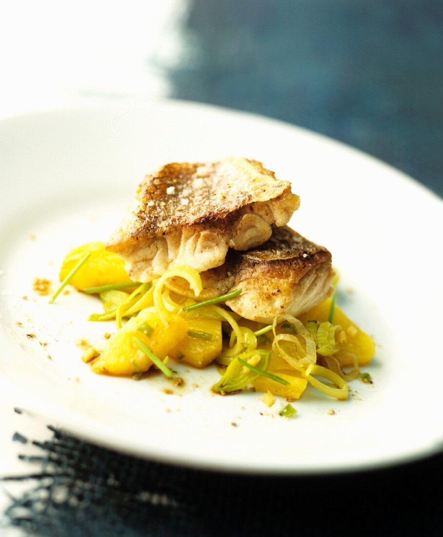 Fried fish fillets on potatoes with leek and pineapple