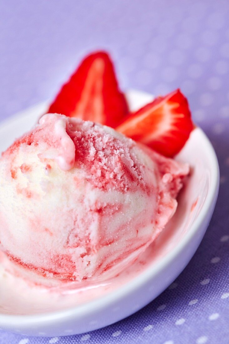 A scoop of frozen yoghurt with strawberries in a shallow dish