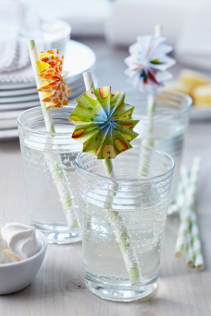 Colourful paper rosettes on drinking straws in glasses