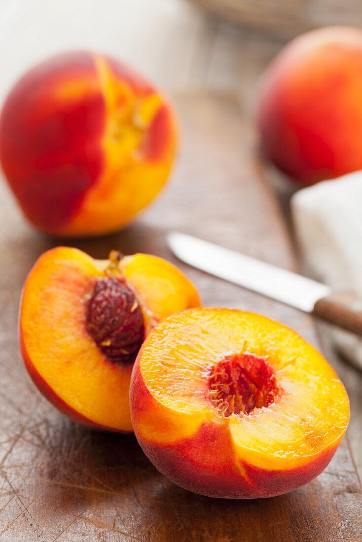 Peaches, whole and halved, on a wooden board with a knife