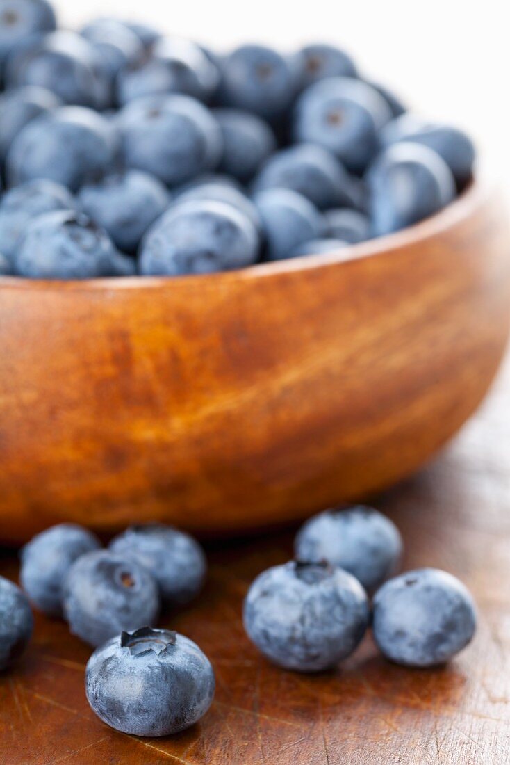 Blueberries in and in front of a wooden bowl