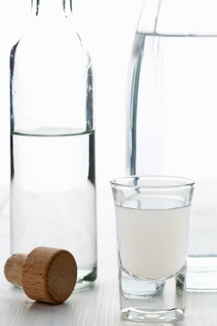 Opaleszierter Ouzo nach Verdünnen mit Wasser mit Ouzo-Flasche und Wasserkaraffe