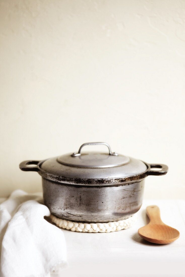 An old cooking pot on a mat with a wooden spoon