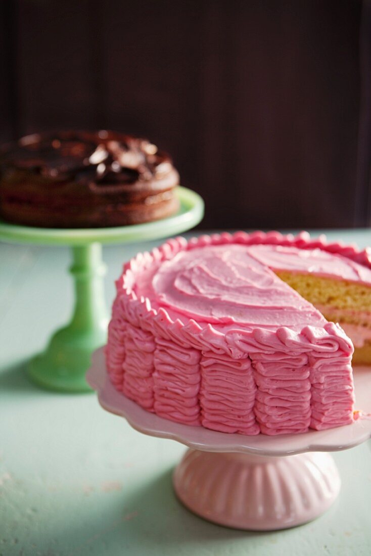 Raspberry layer cake on a cake stand in front of a chocolate layer cake