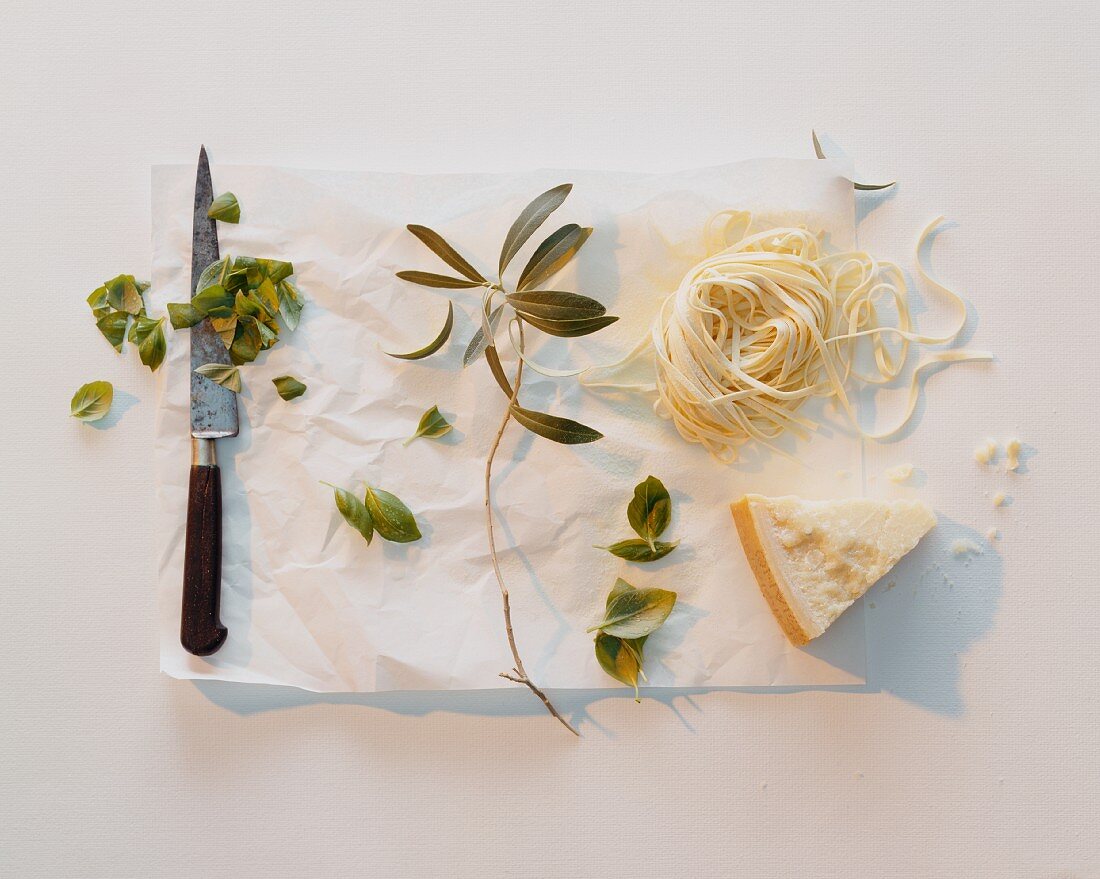 Fresh tagliatelle, parmesan and basil leaves with a knife on paper
