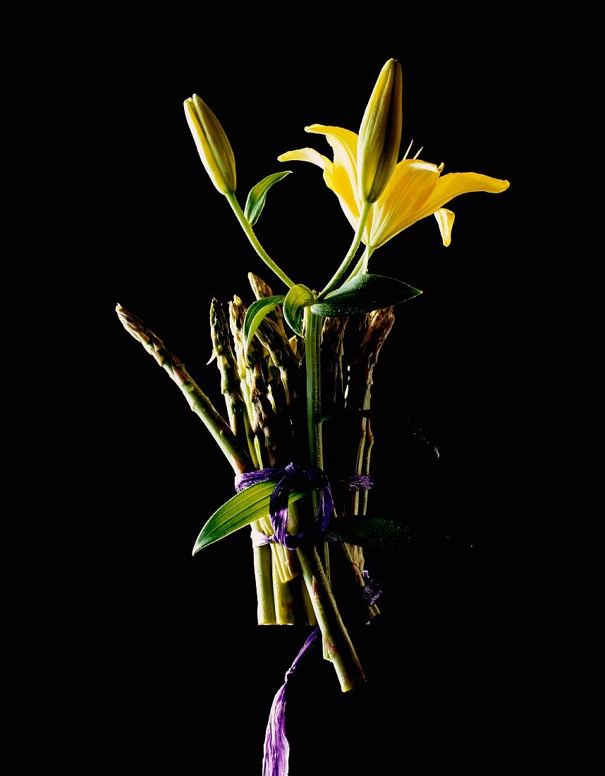 A bunch of green asparagus and yellow lilies against a black background