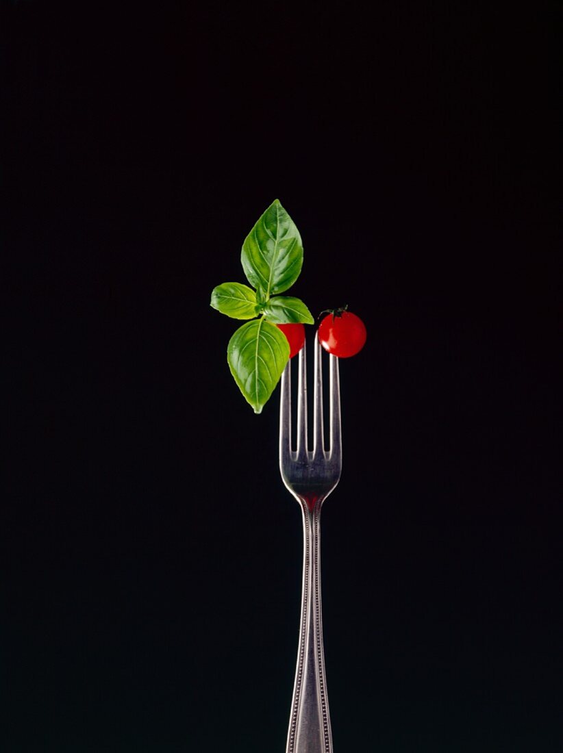 Basil and two cocktail tomatoes skewered on a fork