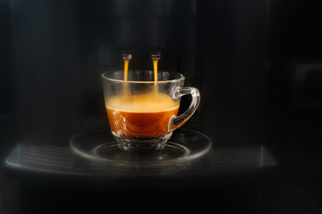 Kaffee fliesst aus der Espressomaschine in eine Glastasse