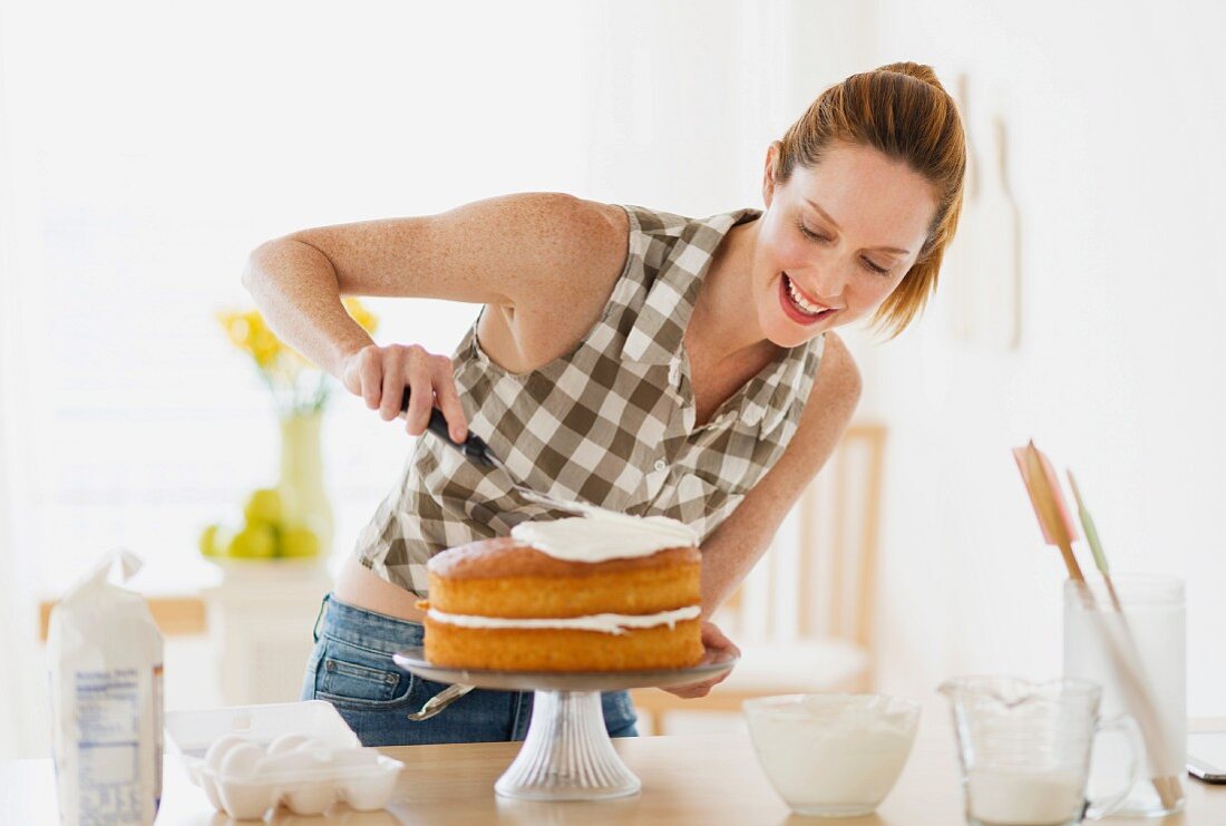 Junge Frau bestreicht Torte mit Creme