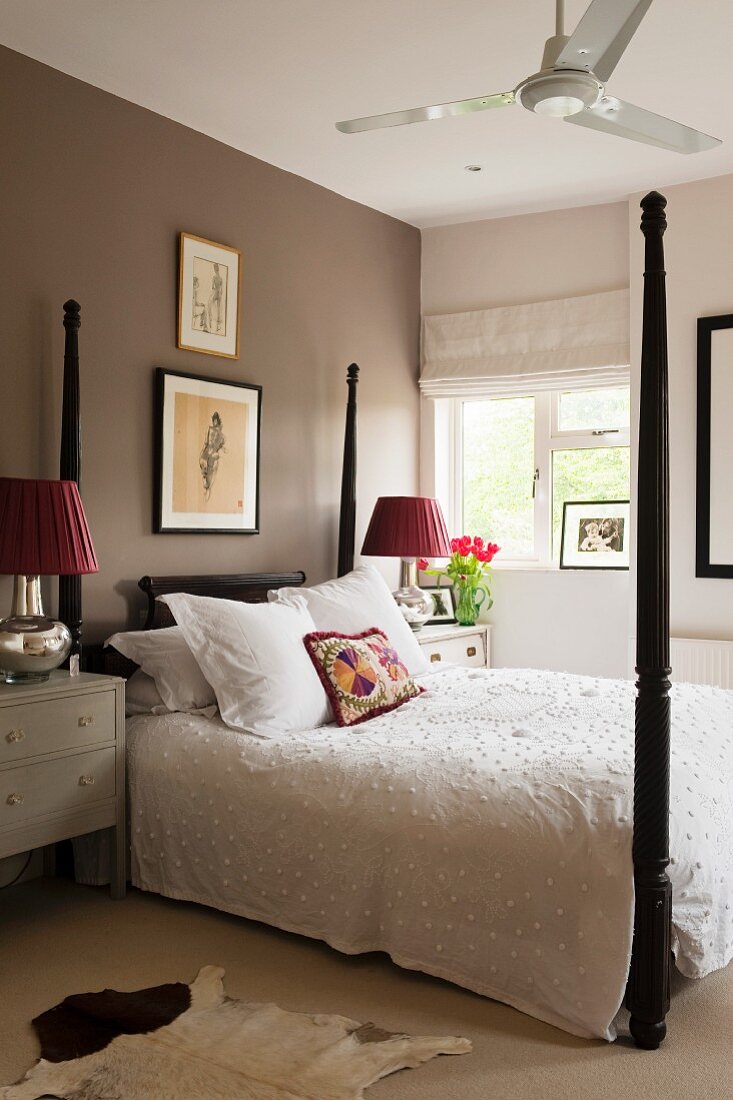 Four-poster bed with dark brown posts and white bedspread below framed pictures on grey-brown wall