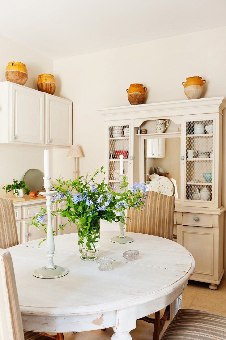 Esszimmer mit Buffetschrank, dekoriert mit Keramiktöpfen im Landhausstil und ovalem Esstisch mit Kerzenständern und Blumenschmuck