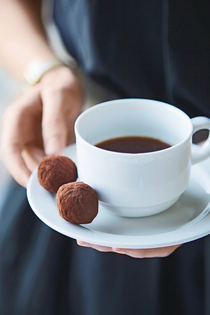 Frau hält Tasse Kaffee mit zwei Schokoladentrüffeln