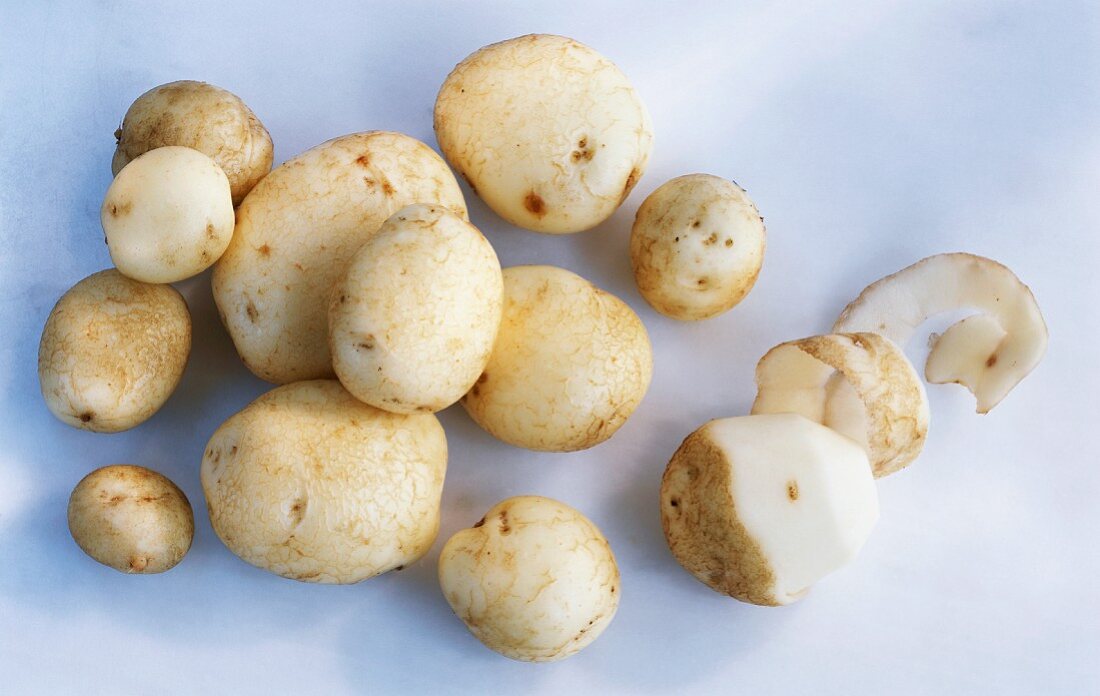 Mehrere Kartoffeln, eine davon halb geschält