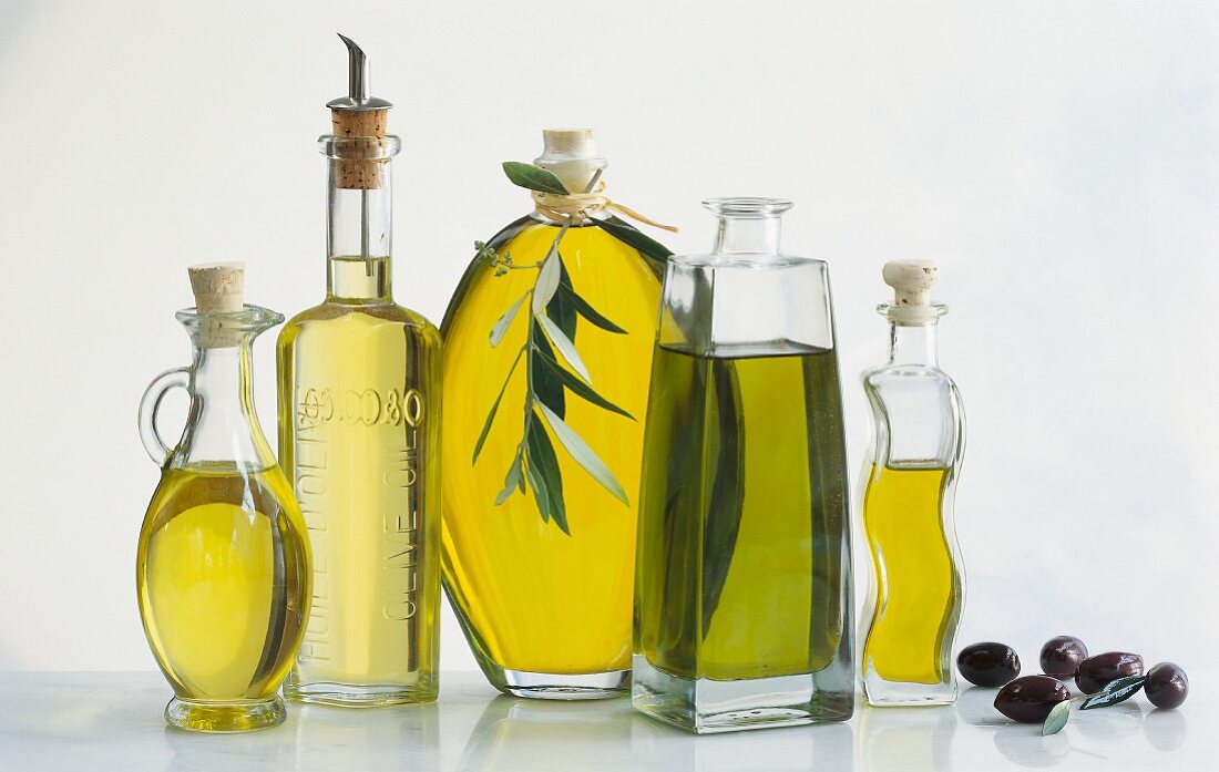 Verschiedene Olivenölflaschen und einige schwarze Oliven