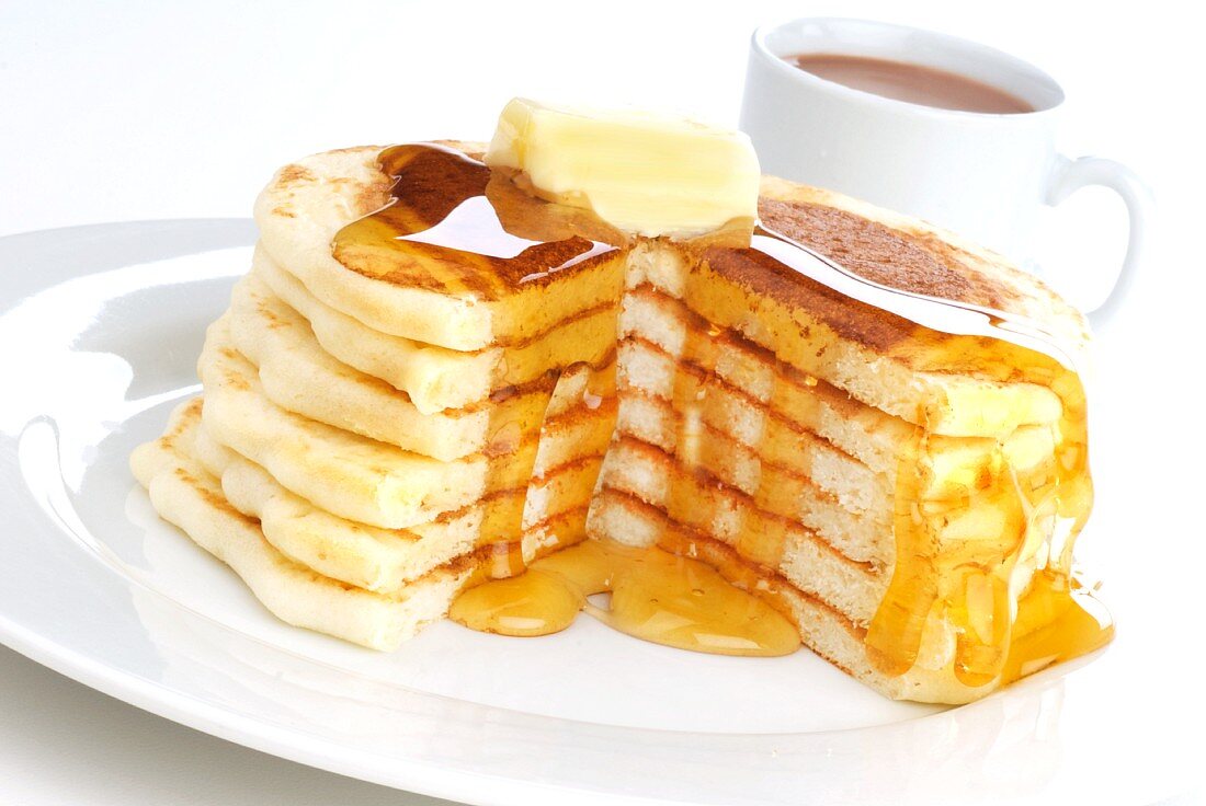 Gestapelte grosse Pancakes mit Butter, Ahornsirup und einer Tasse Kaffee