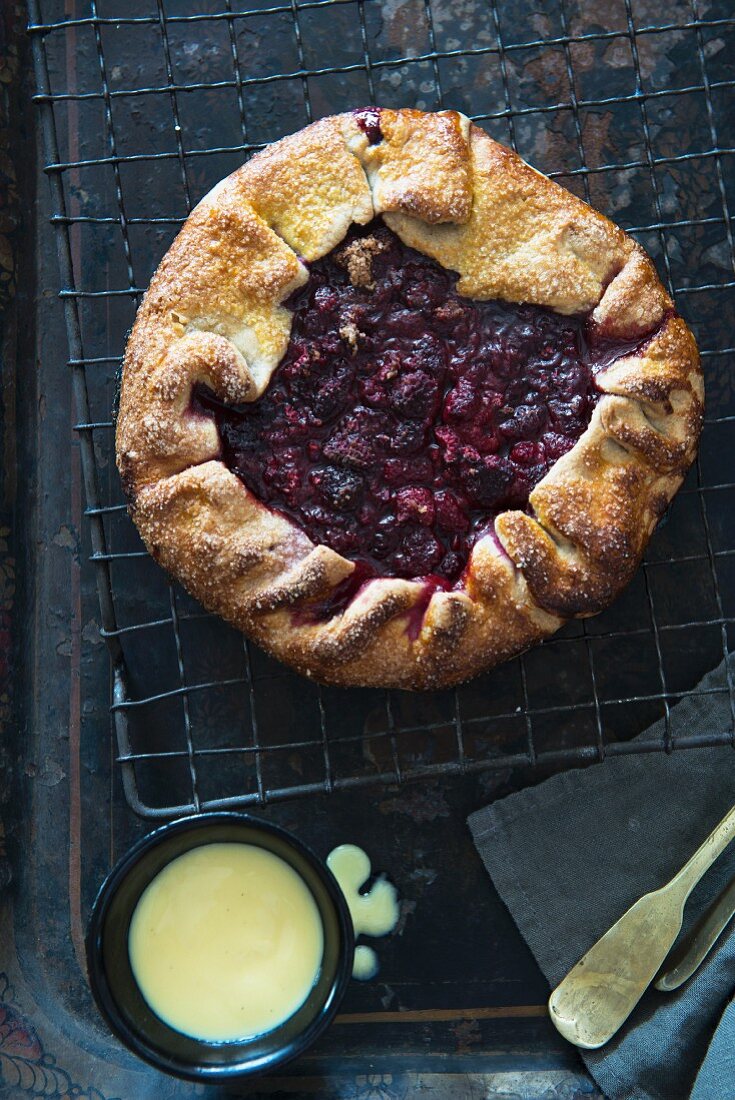 Raspberry galette (a rustic tart) on a cooling rack, and a pot of custard