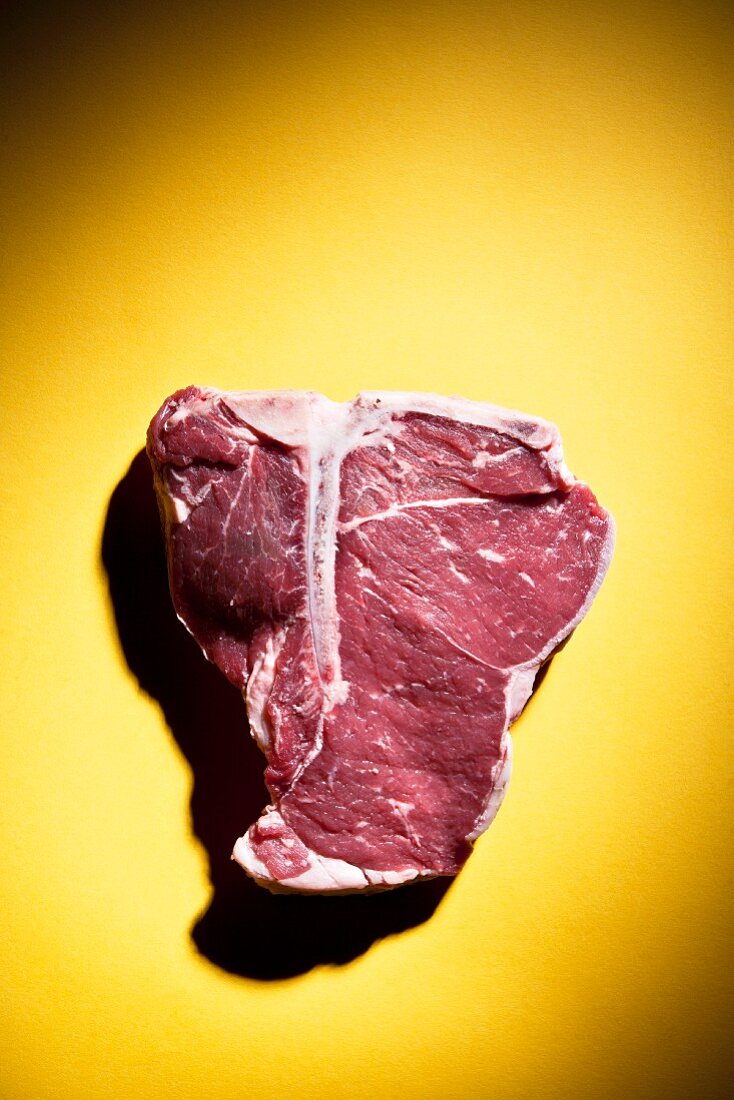 Rohes T-Bone-Steak auf einem gelben Hintergrund