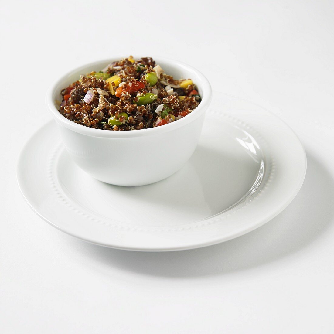 Red Quinoa Salad with Mango, Onion and Soy Beans in a White Bowl on a White Plate