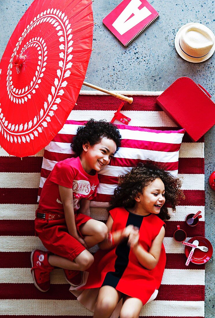 Laughing children dressed in red on red and white striped rug