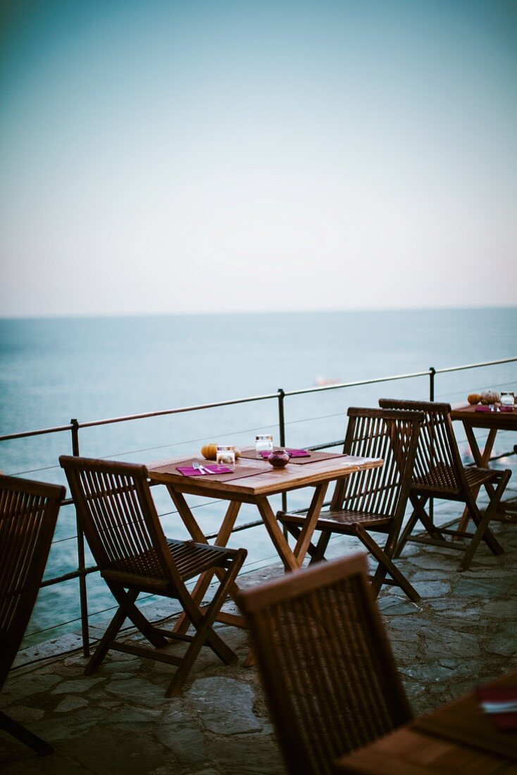 Gedeckte Tische auf einer Terrasse am Meer