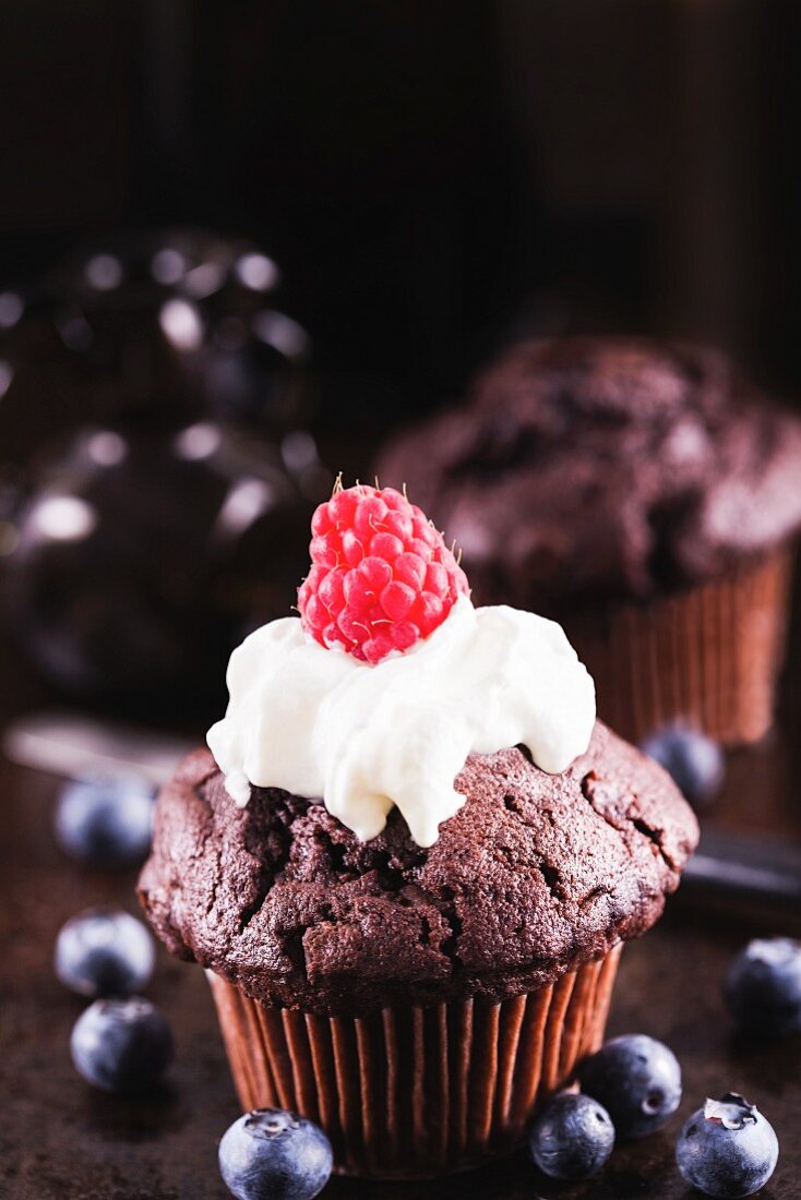 A chocolate cupcake with cream and a raspberry