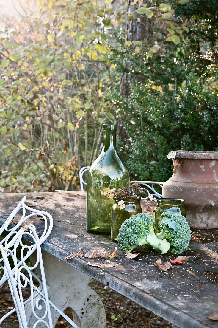 Autumnal still-life of broccoli, jars and urn on stone table in garden