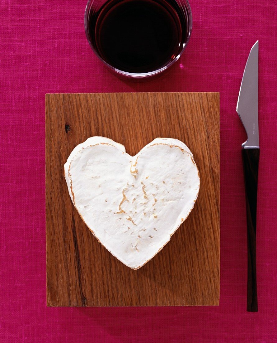 A heart-shaped Camembert, a knife and a glass of red wine