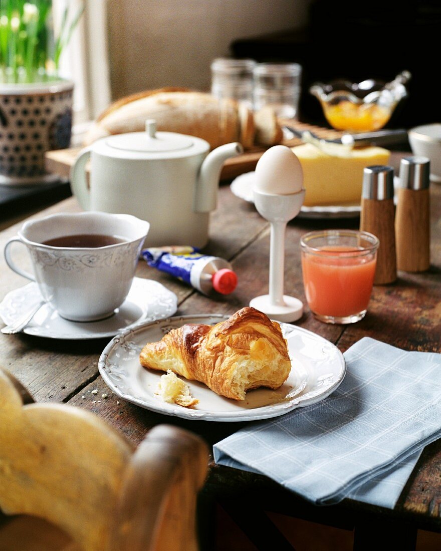 Frühstück mit Croissant, Ei, Saft und Kaffee auf Holztisch