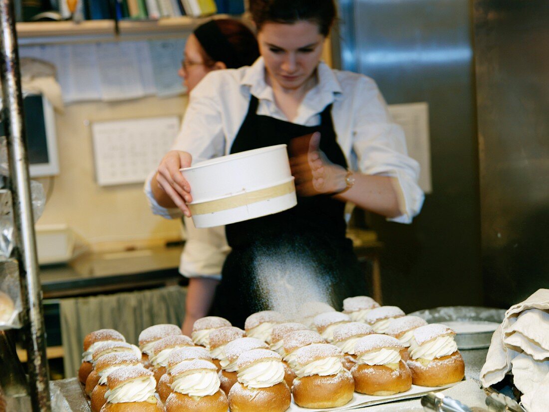Frau streut Puderzucker auf Marzipangebäck mit Sahne in einer Bäckerei