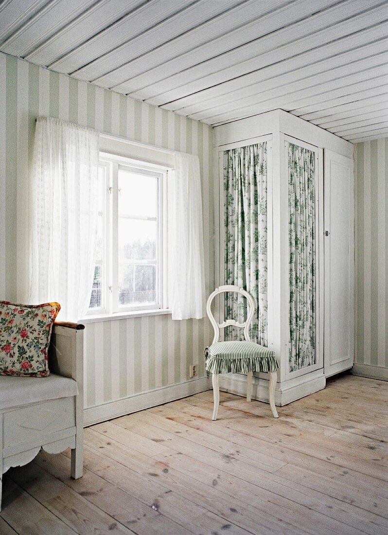 Pale room in Scandinavian wooden house with wide stripes on walls and fitted wardrobe with floral, fabric door panels