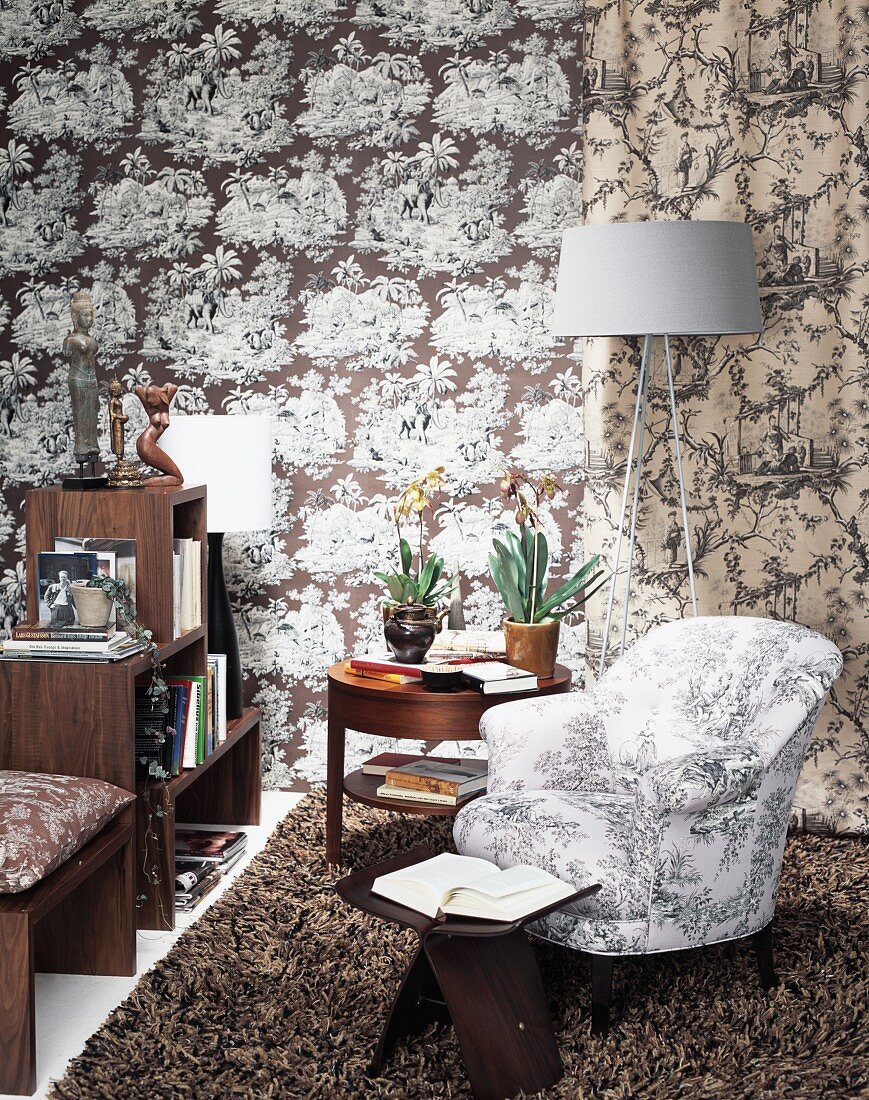 Fifties-style armchair and classic designer stool on flokati rug next to modern standard lamp against wall with patterned wallpaper