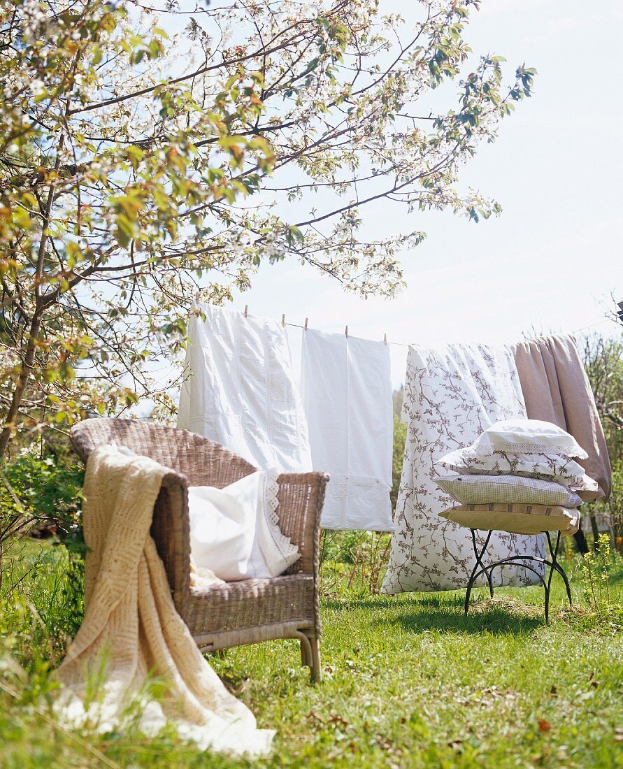 Rattansessel mit Tagesdecke vor aufgehängter Wäsche an Leine im sonnigen Garten