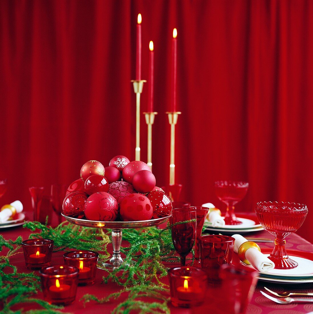 Weihnachtlich gedeckter Tisch mit Kerzenständern vor rotem geschlossenem Vorhang