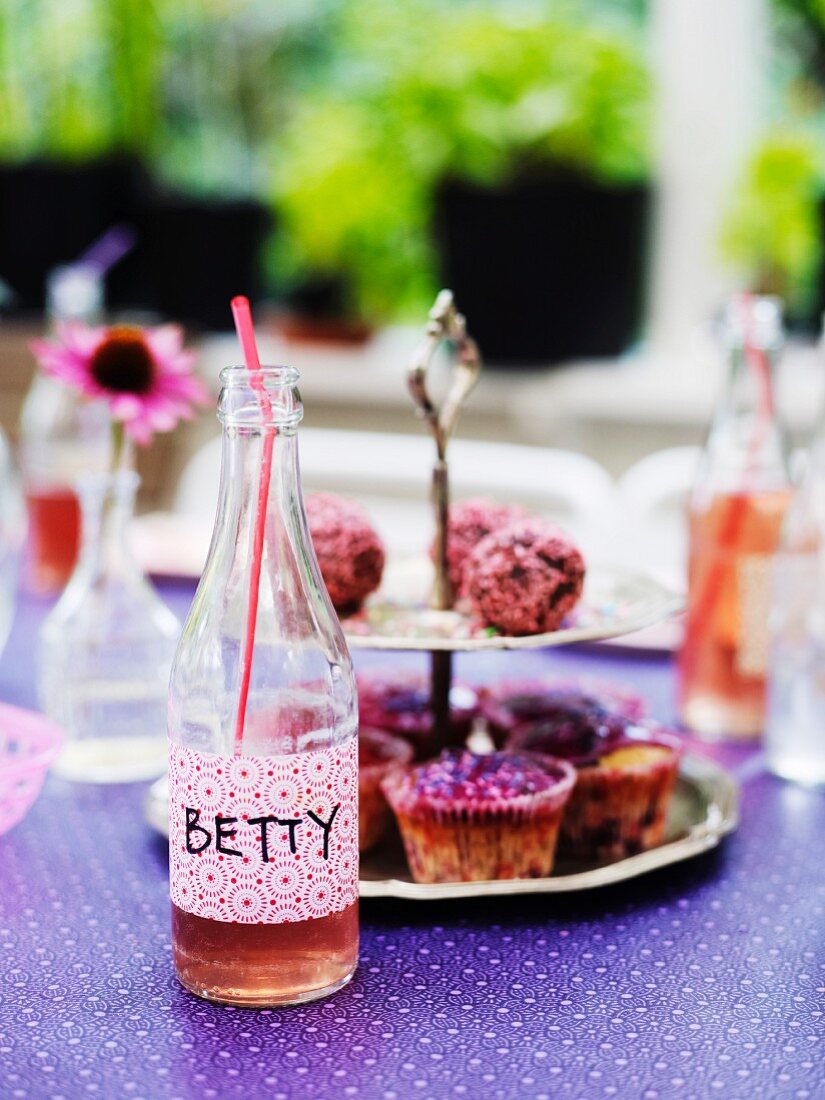 Bottle with lemonade and cupcakes on table