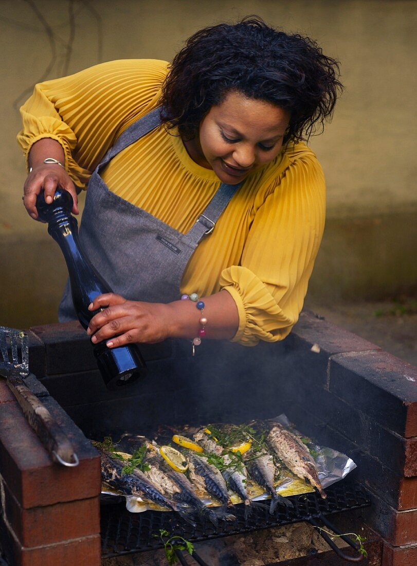 Frau würzt Fisch auf dem Grill mit Pfeffer aus der Pfeffermühle