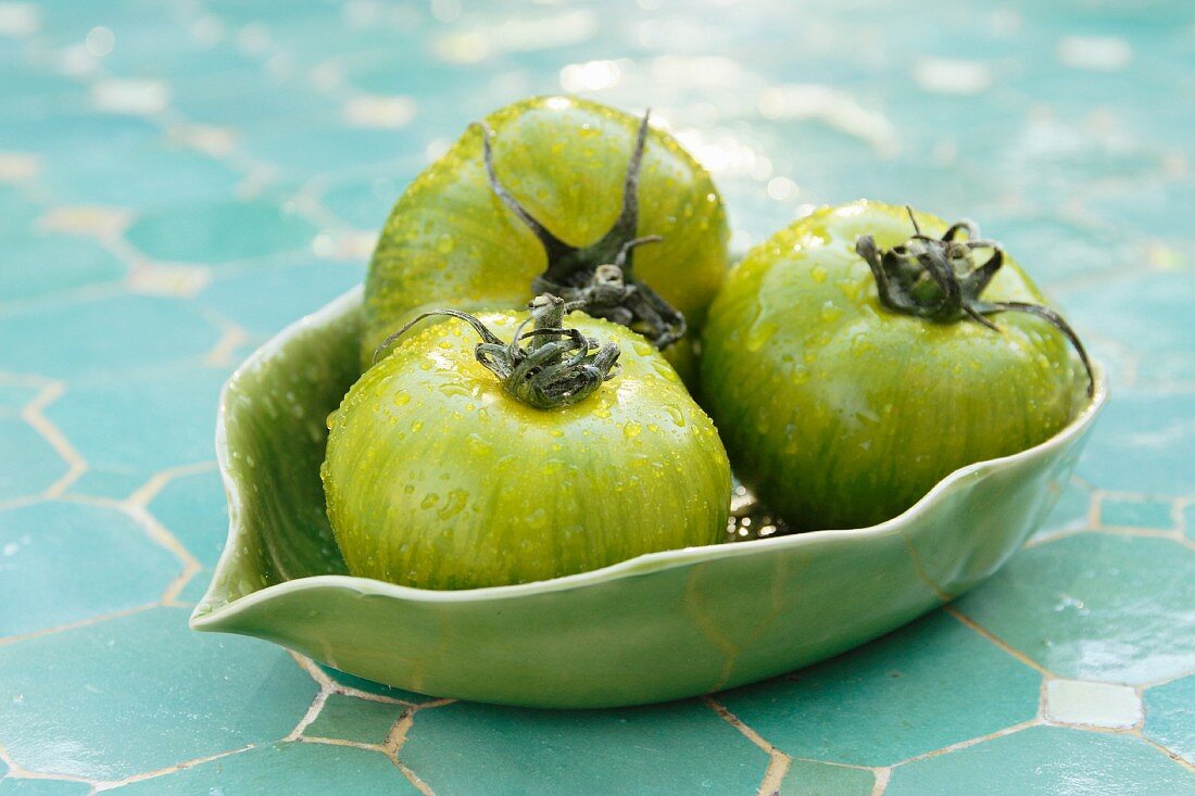 Three green tomatoes with water droplets in a ceramic dish