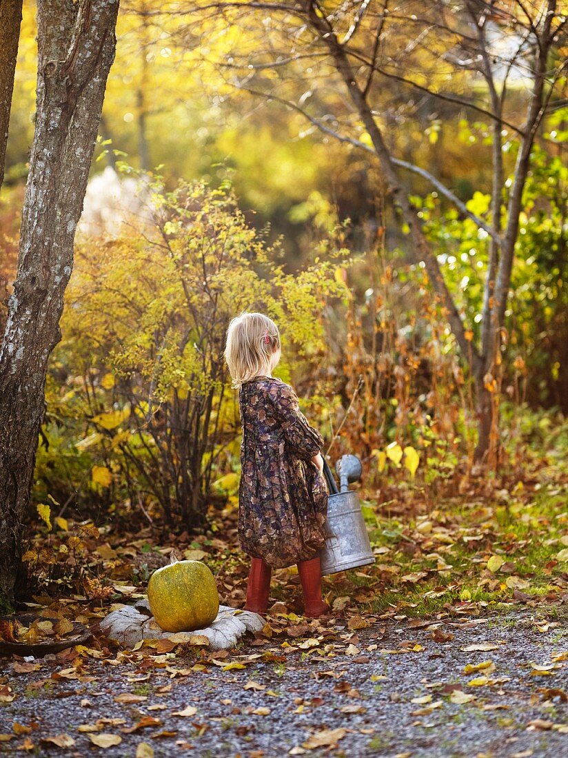 Little girl with watering can in autumnal garden