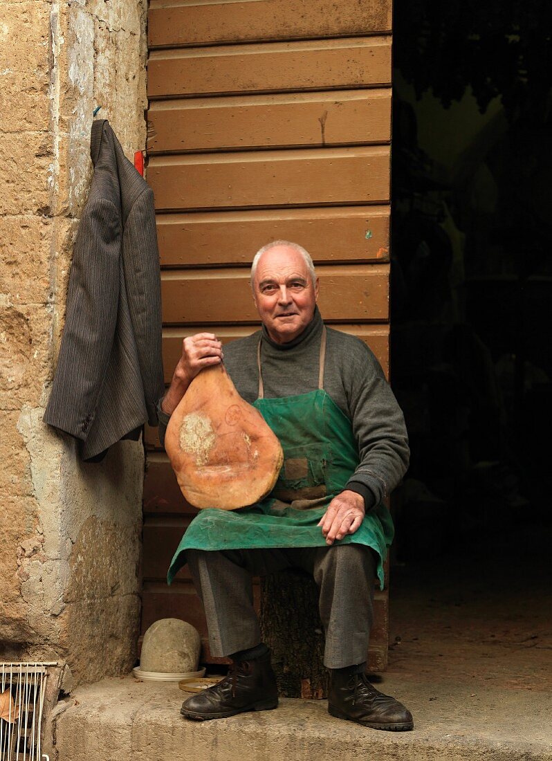 Italy, Tuscany, senior man holding traditional homemade ham
