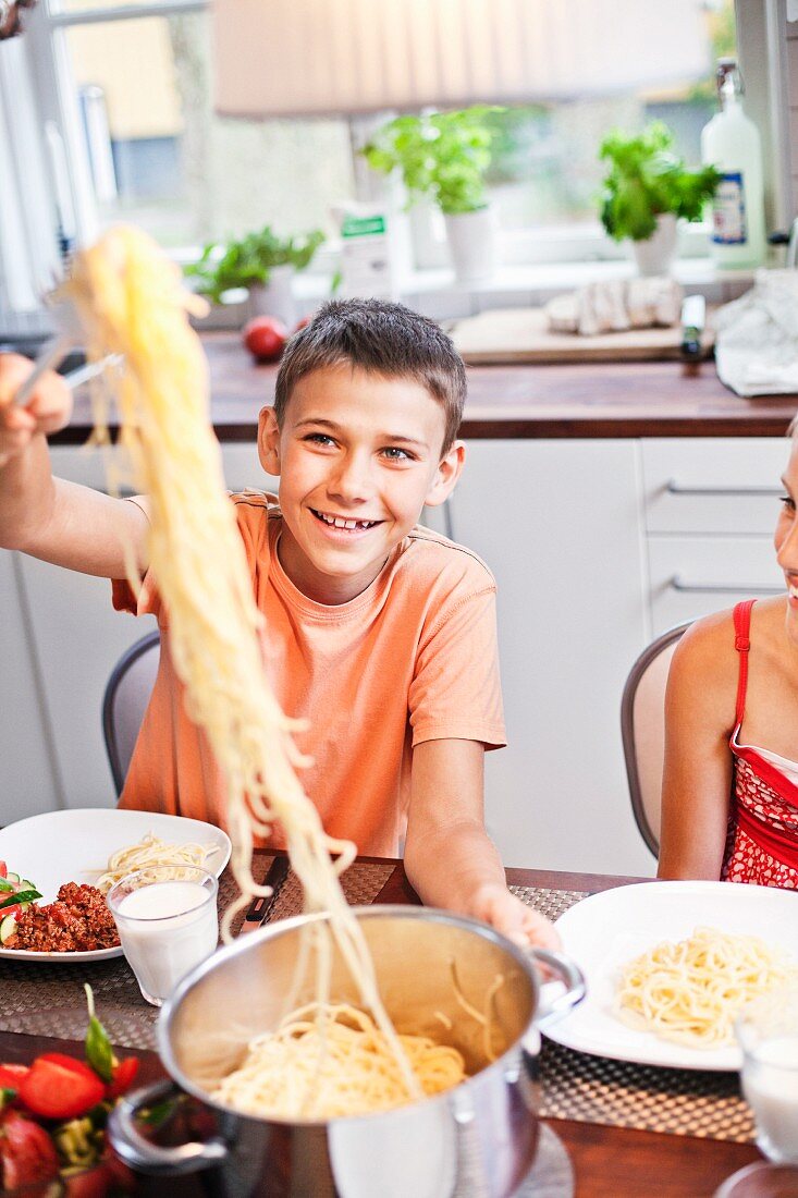 Junge nimmt sich Spaghetti aus dem Kochtopf