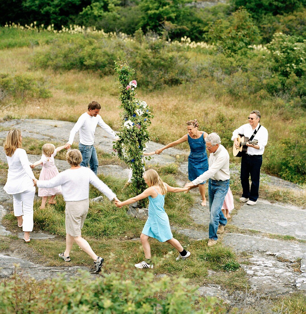 Sommerlich gekleidete Menschen tanzen singend um einen Maibaum