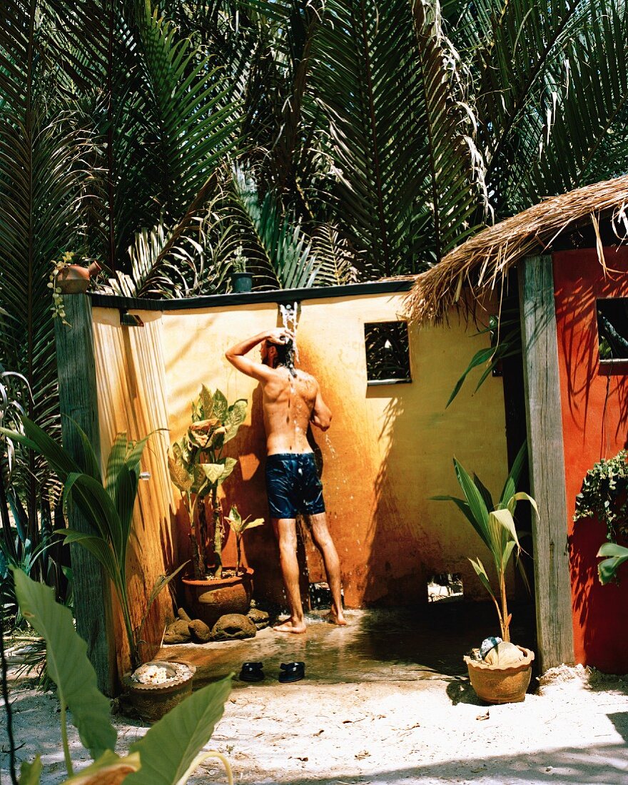 Mann in gemauerter Dusche unter freiem Himmel, umgeben von tropischen Pflanzen