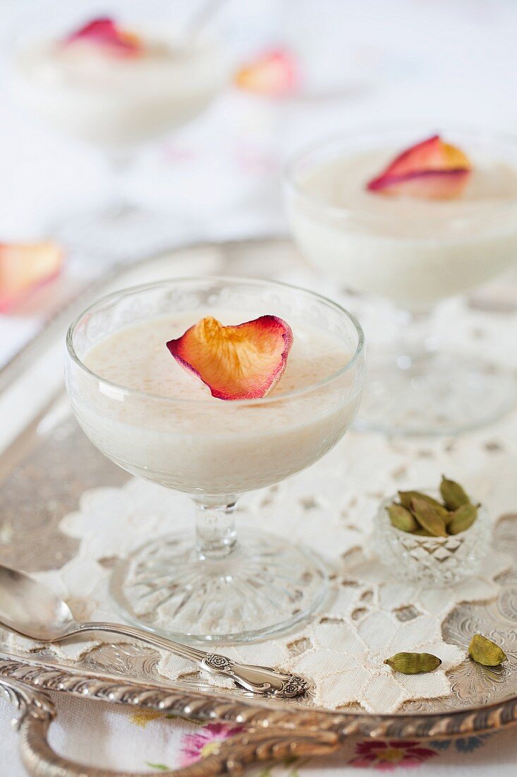 Almond rice pudding with rose petals and cardamom seeds on a silver tray