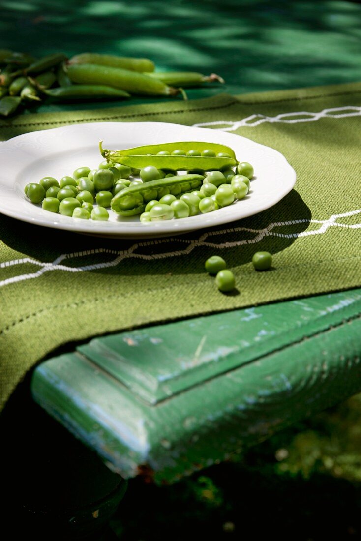 Peas (organic), partly podded, with whole pods on a plate and on a table