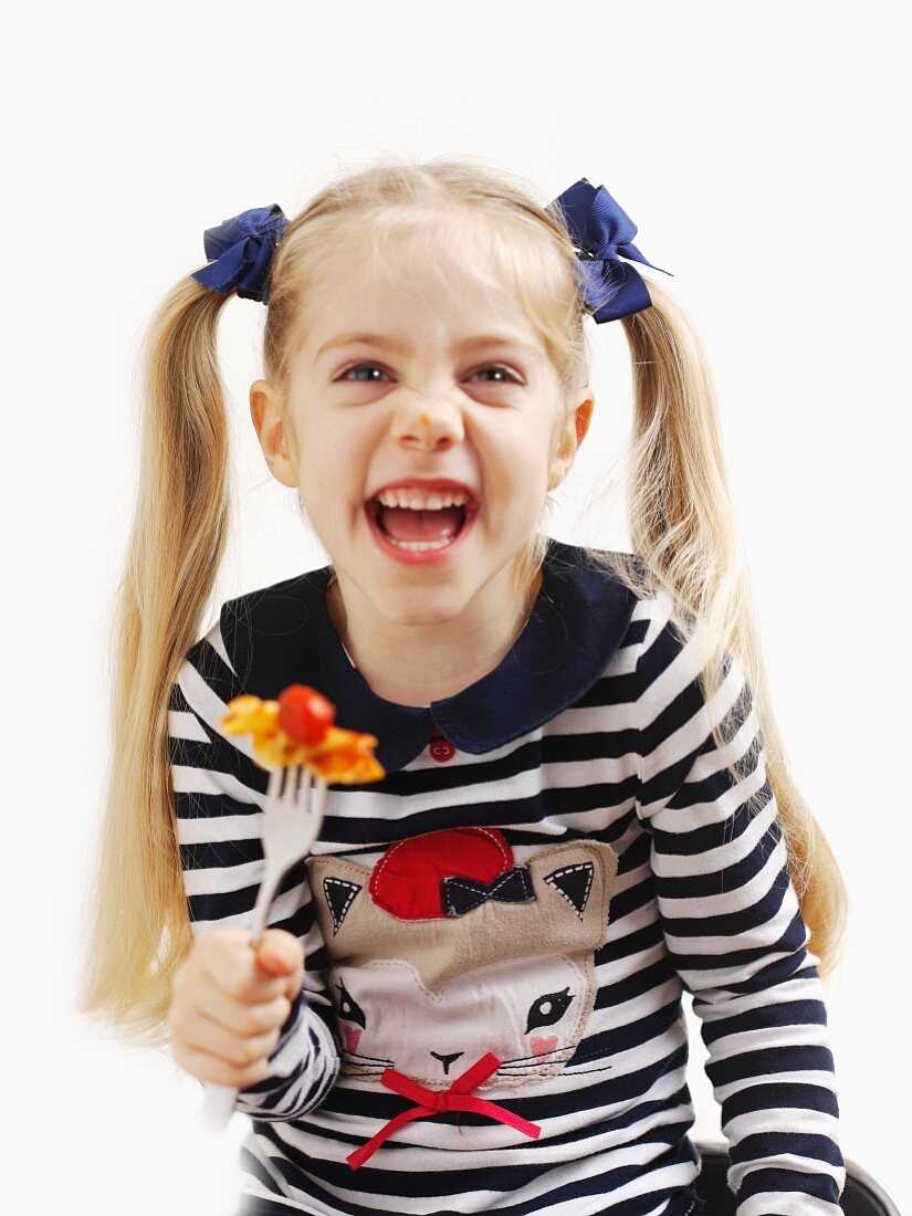 A small girl holding a fork with pasta and tomato