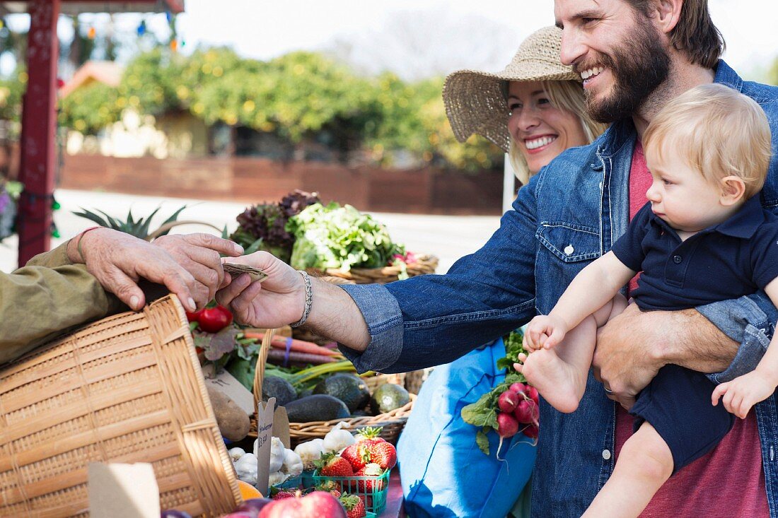 Familie mit kleinem Kind kauft Gemüse auf Markt
