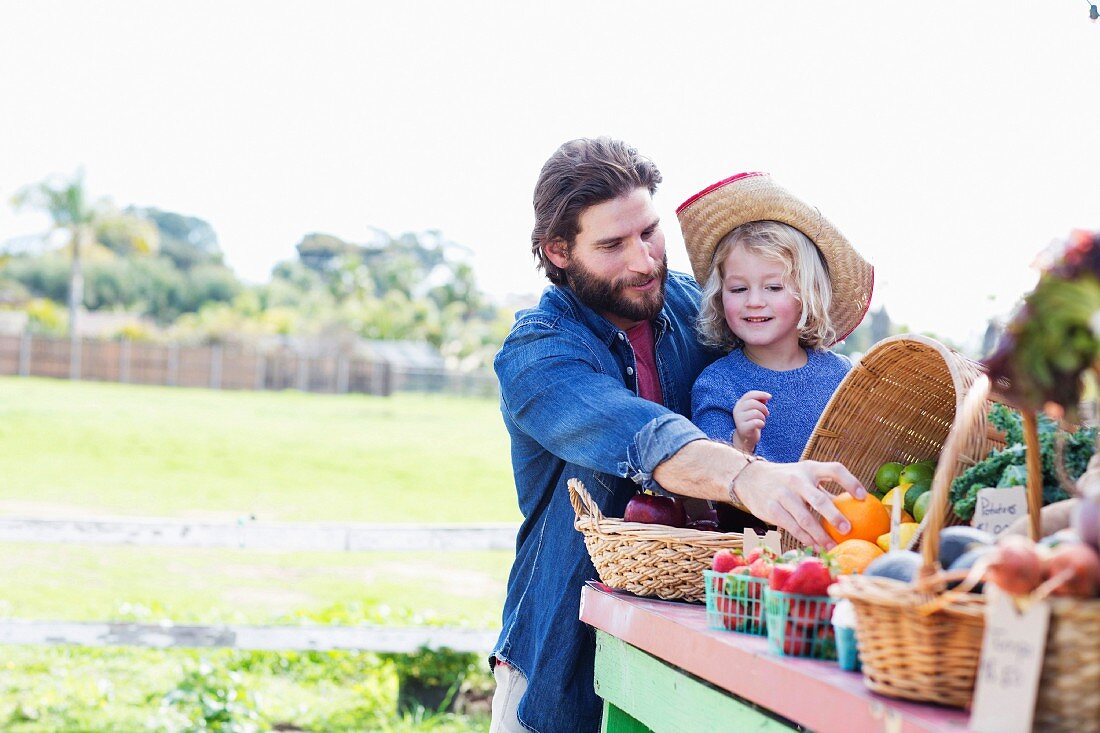 A father and daughter at a stall at a farmer's market with fresh fruit and vegetables