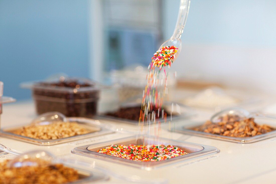 Colourful sugar sprinkles tipping from a spoon into a container